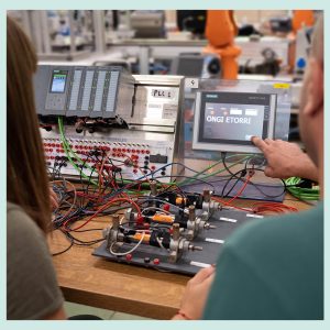 Dos alumnos colaborando en un aula, trabajando en proyectos de sistemas de automatización industrial, rodeados de PLC, materiales y herramientas técnicas