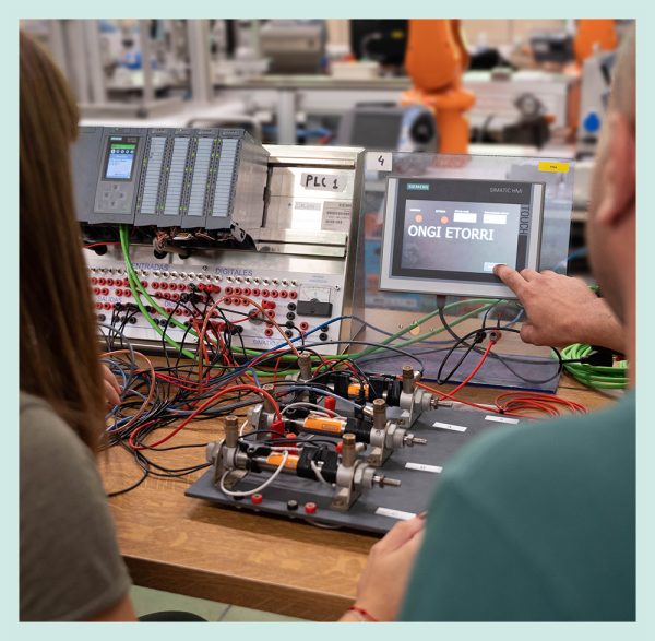 Dos alumnos colaborando en un aula, trabajando en proyectos de sistemas de automatización industrial, rodeados de PLC, materiales y herramientas técnicas